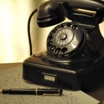 Un téléphone noir ancien un stylo et du papier griffonné sur un bureau