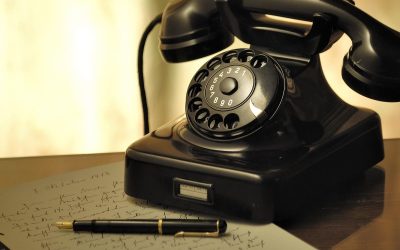 Un téléphone noir ancien un stylo et du papier griffonné sur un bureau