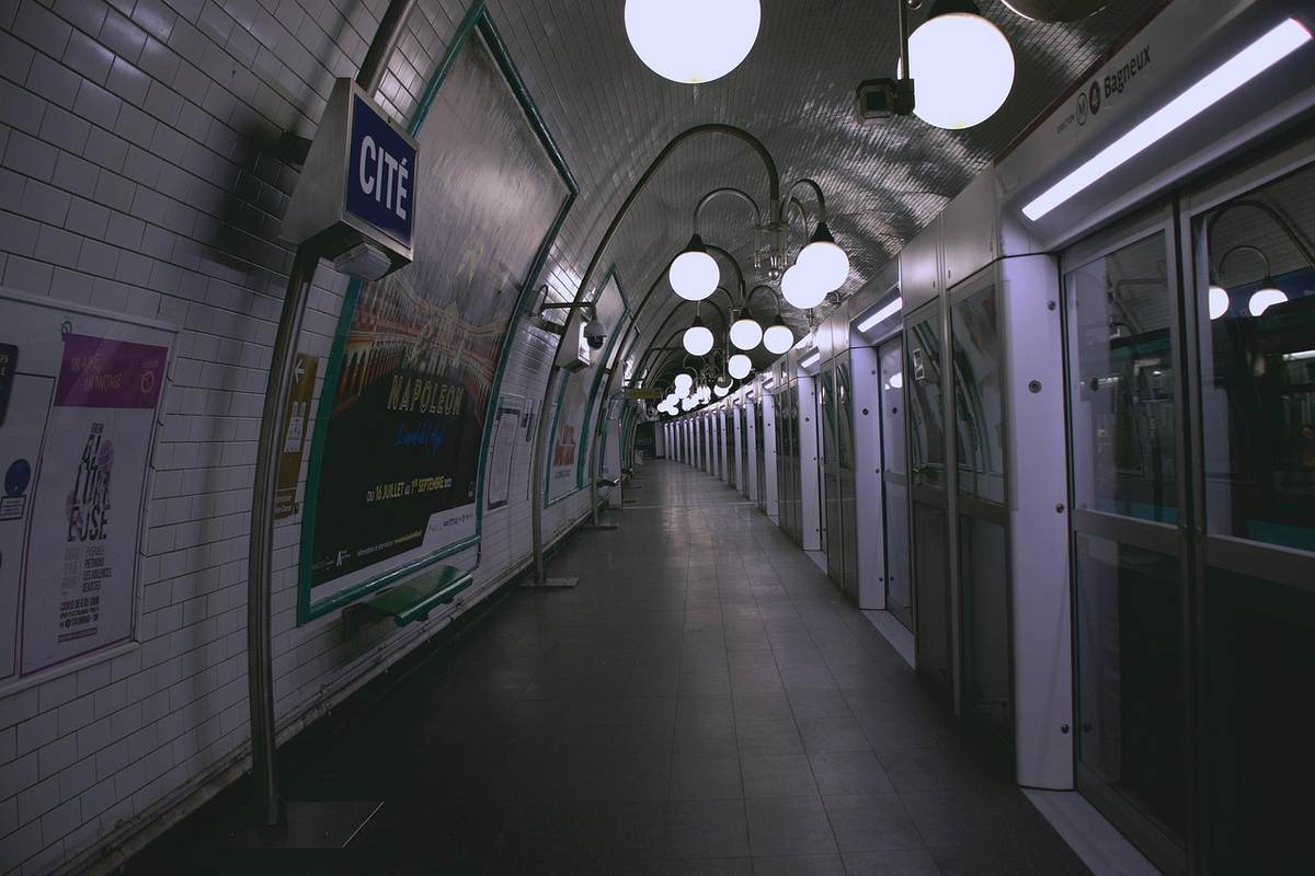 Couloir souterrain de station de métro parisien désert, illuminé par des lampadaires, panneaux publicitaires sur les murs